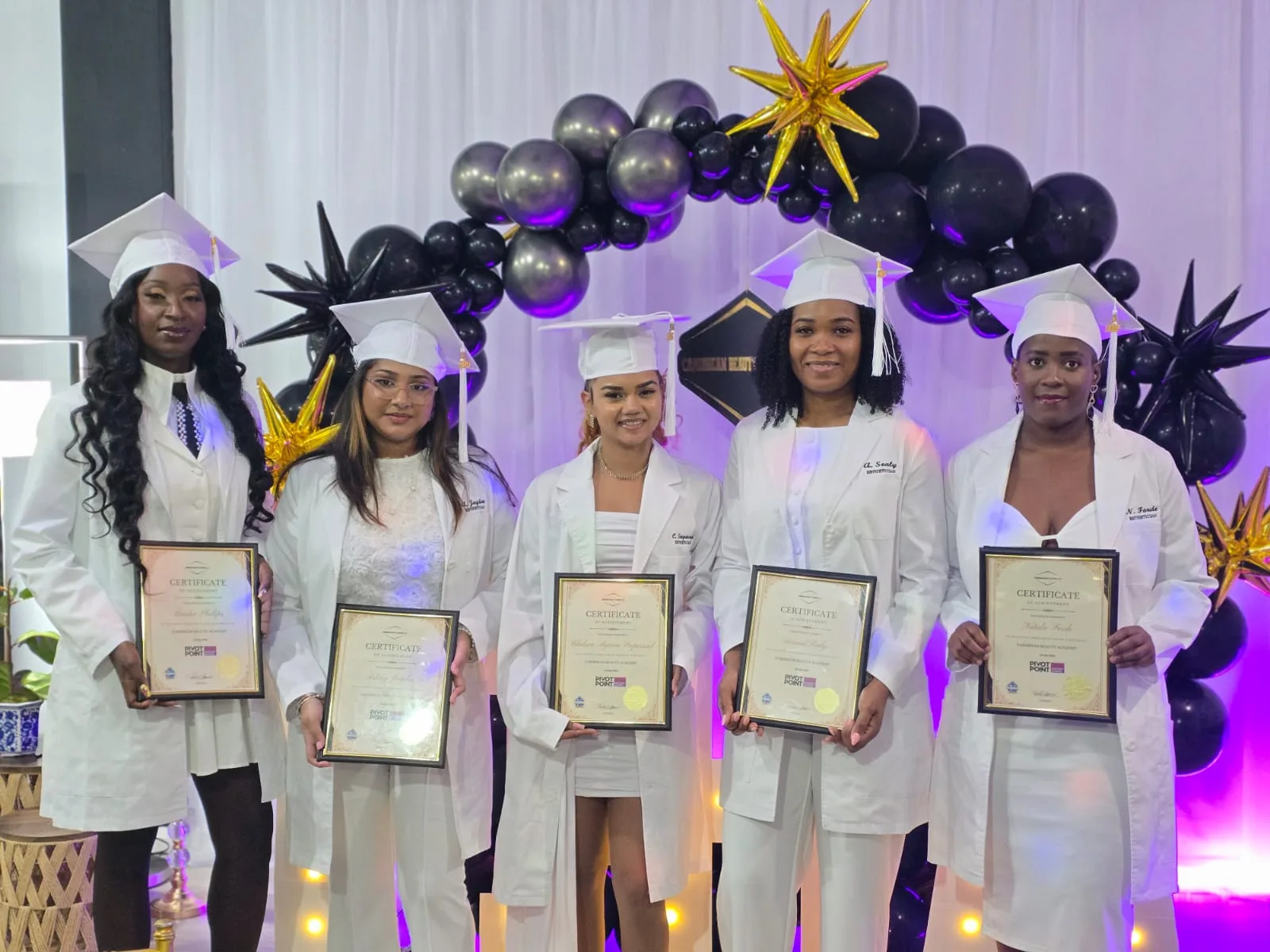 Five graduates in white coats holding their Pivot Point certificates of achievement